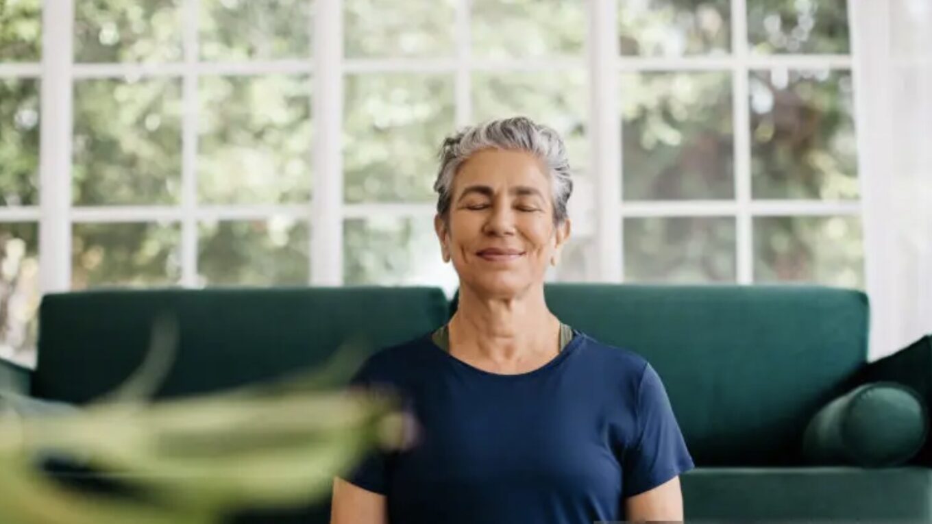 Mulher madura praticando meditação em casa, com expressão serena, simbolizando equilíbrio mental e bem-estar para um emagrecimento saudável.