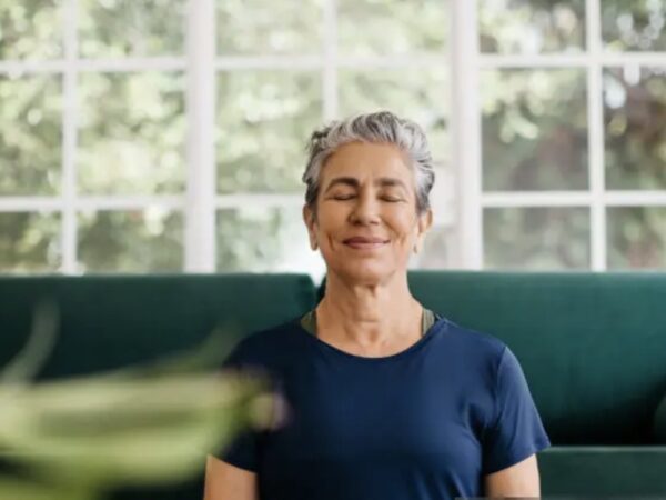 Mulher madura praticando meditação em casa, com expressão serena, simbolizando equilíbrio mental e bem-estar para um emagrecimento saudável.